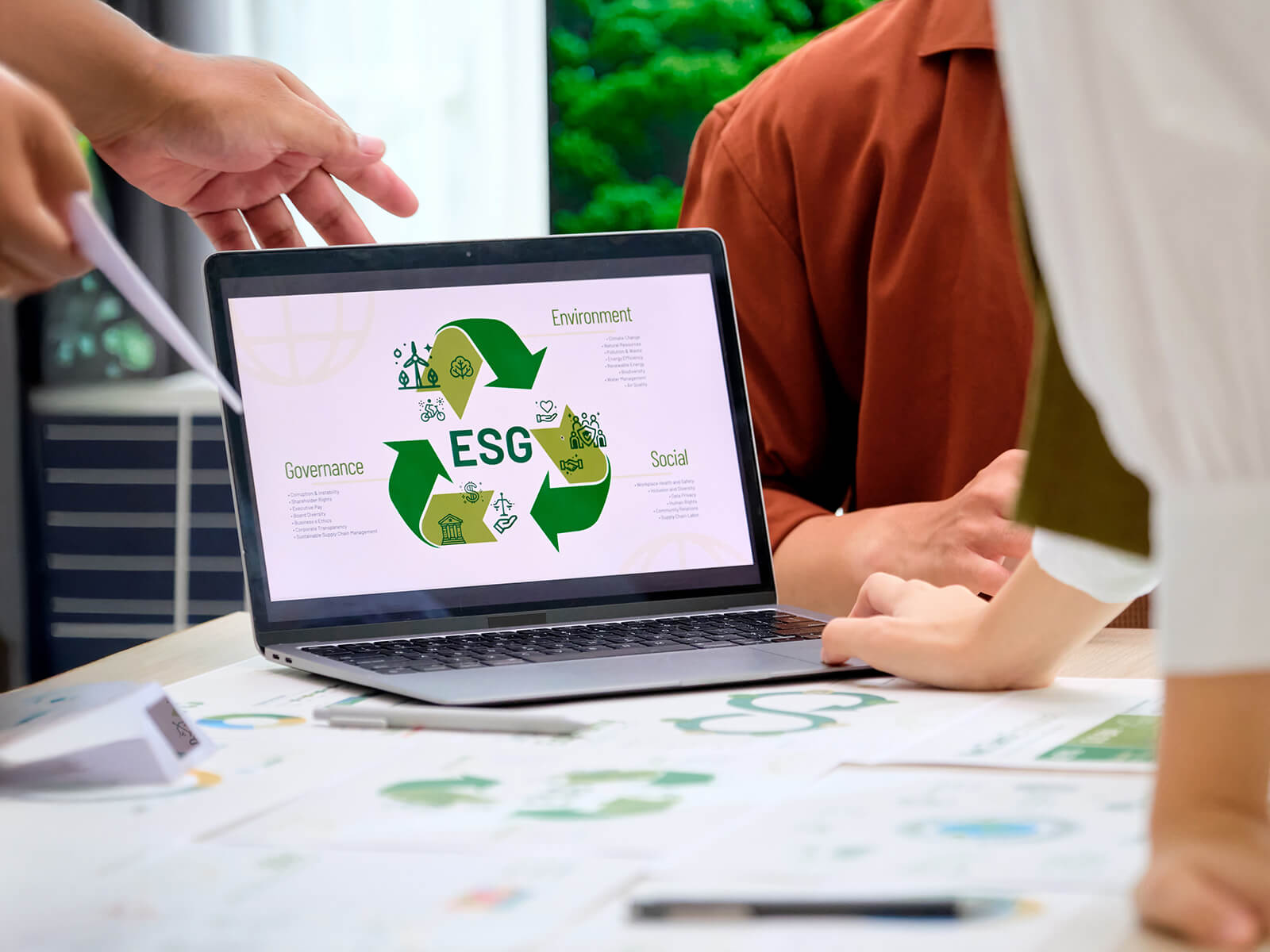 Bærbar computer på et skriveborg. Skærmen viser en bæredygtighedsillustration og teksten "ESG"